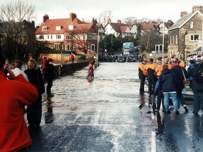 The flooding of the bridge in April 2002 when the River Wharfe broke its banks. People wade through the water, cars and lorries queue up unable to cross and men in orange and black wetsuits prepare a rubber dingy.