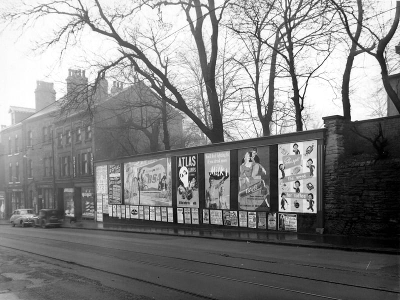 The West side of Harrogate Road showing posters advertising 'Sharp's Toffee', 'Carol's Chocolate', 'Milk', 'Atlas Lamps', 'BSA Bicycles' and various theatres. Cars are parked outside Ainsleys Bakery further down the road. Tramtracks are visible. Pictured in December 1954.