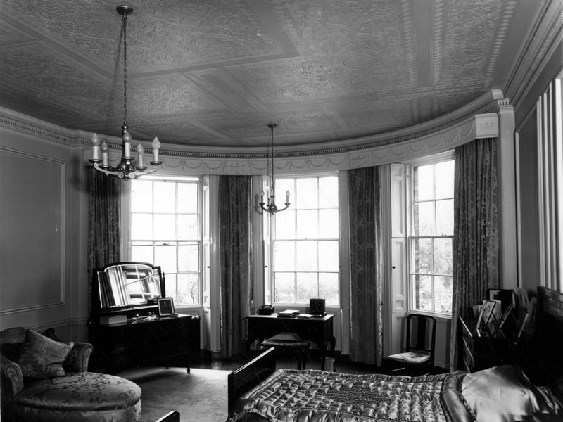 Inside a bedroom at Allerton Hall with a large bay window in the main hall, built originally in the 18th century. Mouldings around room and window with sash window casing, and the ceiling is plastered in symmetrical patterns.