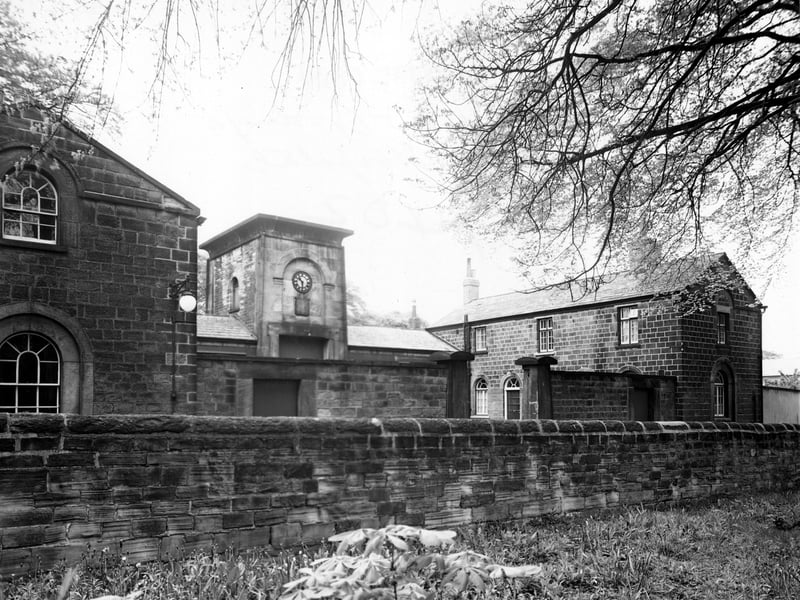 Stables on Gledhow Park Drive. The centre building has a clock on the front. A stone wall and field are in the foreground. A lamp is on the side of a building and large stone gateposts are visible. It was in the grounds of the former Chapel Allerton Hospital. Pictured in May 1950.