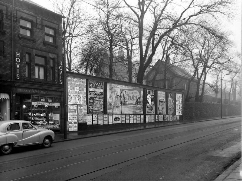The west side of Harrogate Road in December 1954 showing number 71, Ainsleys Bakery. A car is parked on the left. Advertising posters for Grand Theatre, Forum Cinema, Theatre Royal, BSA Bicycles, Atlas Lamps, Milk, Carols Chocolate and Sharps toffee are visible, among other small ones. Tram tracks and cobbles are visible.