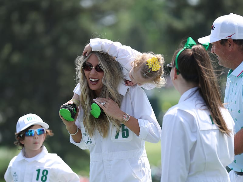 Kelley Cahill, wife of Jon Rahm,, walks with their daughter Alaia Cahill Rahm as Patrick Reed of the United States and children look on.