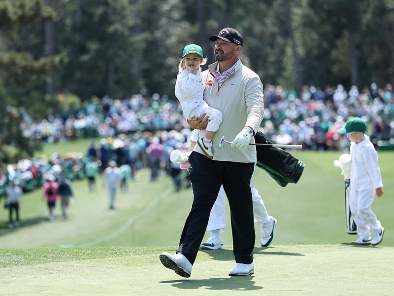 Amateur Brandon Holtz of the United States carries his daughter Millie Holtz across the second green.