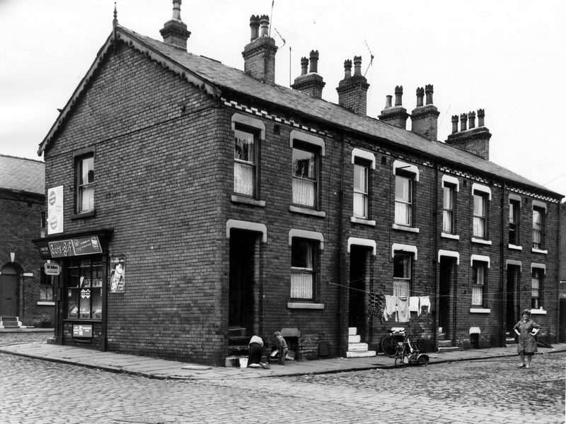 On the left edge, Ledsham Terrace can be seen, this is looking from Gordon Road. The corners grocers shop is the business of J. Walton. A woman is cleaning the steps of number 18 Ledsham Grove, next 16 has a bike and child's bicycle outside. Pictured in June 1964.