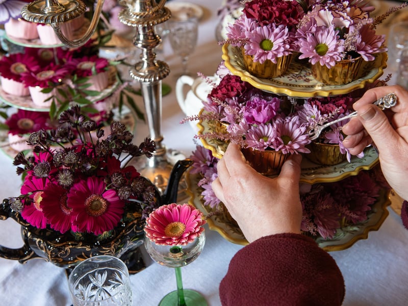 A small dining table has been filled with whimsical pots, cake stands and cups all intricately decorated with fresh cut flowers.