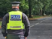 A police officer guards the junction of Whirlowdale Road and Abbey Lane. In the distance is a cluster of police vehicles close to the scene of the murder investigation in Ecclesall Woods.