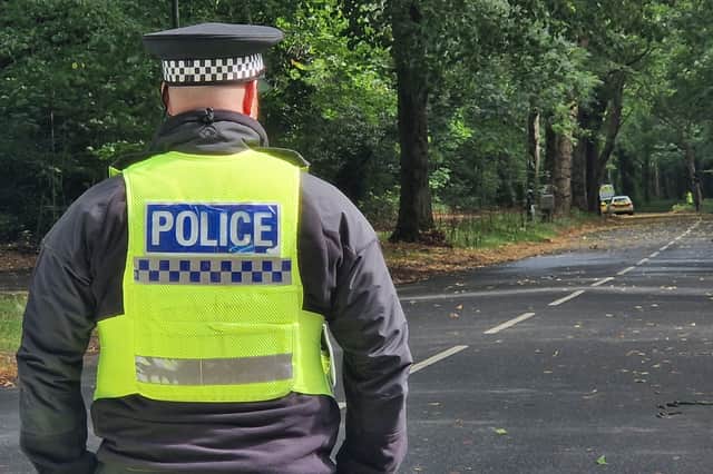 A police officer guards the junction of Whirlowdale Road and Abbey Lane. In the distance is a cluster of police vehicles close to the scene of the murder investigation in Ecclesall Woods.