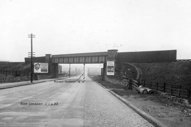 Railway bridge running over Gelderd Road. On the left hand side is a big billboard for Oxo with a big picture of Henry VIII and the message; 'Henry VIII had six wives - your home comfort is Oxo.'