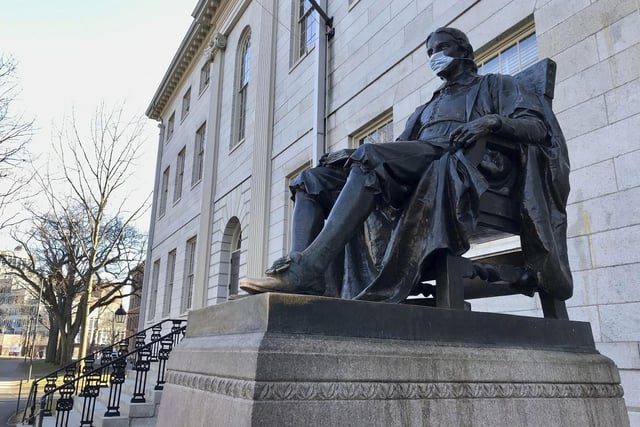 The John Harvard statue at Harvard University, a popular tourist attraction, sits adorned with a medical mask.