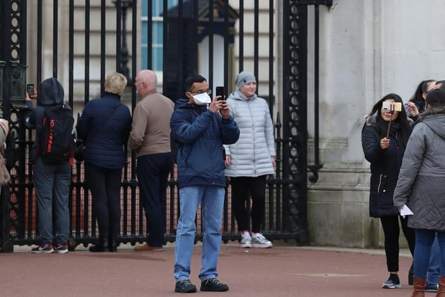A tourist wearing a face mask to protect against the spread of coronavirus takes a selfie outside of Buckingham Palace.