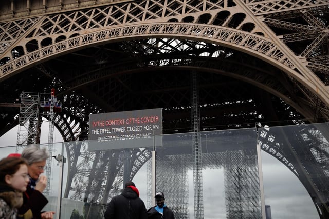 People walk past a screen announcing the closure of the Eiffel Tower in Paris.