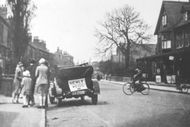 Looking west along Austhorpe Road. An open-top car has a sign saying 'Newly Weds' on the back. A group of people, possibly from the wedding party, are standing at the side.
