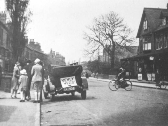 Looking west along Austhorpe Road. An open-top car has a sign saying 'Newly Weds' on the back. A group of people, possibly from the wedding party, are standing at the side.