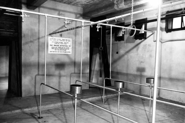 The shower room in the wash-house on South Brook Street in Hunslet. The framework of the shower units with soap bowls attached are visible. Instructions for washing are on the back wall.
