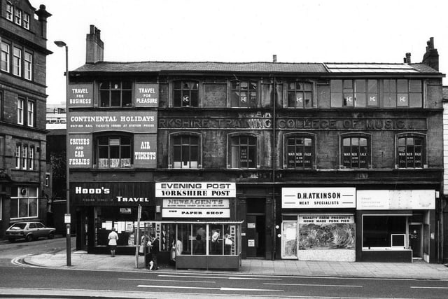 On the left is the Jubilee pub. The row of shops has stone lettering above second floor 'Yorkshire Training College of Music'. The shops are, Hoods Travel, The Paper Shop newsagents, D.H. Atkinson butcher and a vacant store.