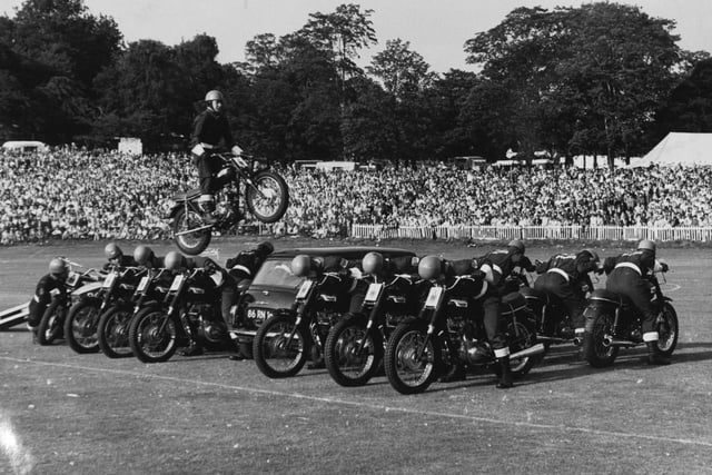 A member of the Rotal Marines Motor-cycle Display Team performs a spectacular leap over 14 men and a mini car at Leeds Gala at Roundhay Park.