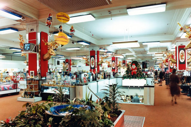 Christmas displays in the Perfumery department. A fountain with tropical plants is in the foreground and there are gold reindeer heads above the merchandise.