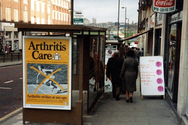 Eastgate looking east. A bus shelter in the centre of the picture has an advert for Arthritis Care. On the right, Number 18 Coffee Bar has a menu board outside.