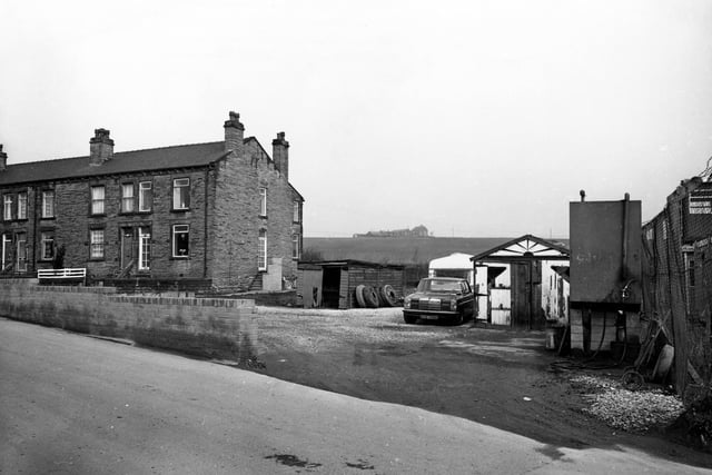 This view shows part of Woodview Terrace, a short terrace of houses on Quarry Lane, Woodkirk. On the right is a yard with a car, a caravan, a garage and a shed with tyres piled up against it.