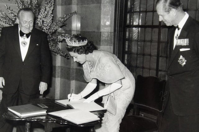 The Queen watched by Prince Philip and the Lord Mayor of Leeds, Coun William Hudson, signs the visitors' book at Leeds Civic Hall.