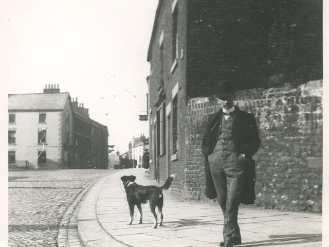 A man and his dog posing for a picture in Queens Square close to the junction with Chapel Street. Beyond is the Bull Hotel with its distinctive sign profile.