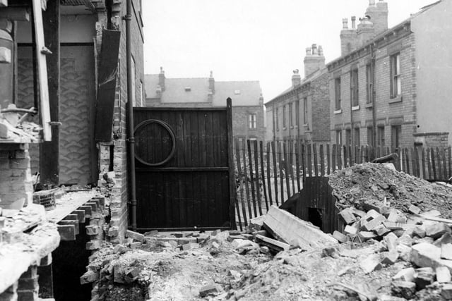 The back garden of a house on Fairfield Crescent in Bramley with extensive bomb damage. There is an Anderson shelter in front of a wooden fence.
