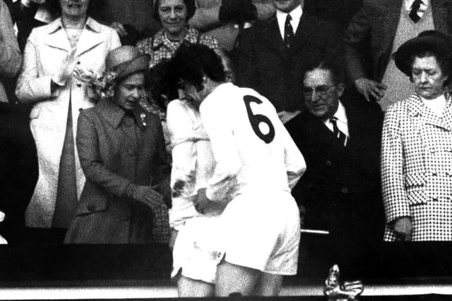 Mick Jones is helped up the steps by Norman Hunter to receive his winners' medal.