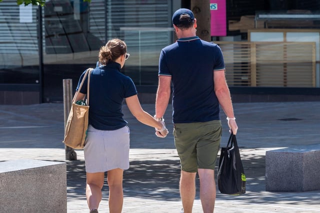 A couple wearing plastic gloves as they walk through Leeds city centre after food shopping.