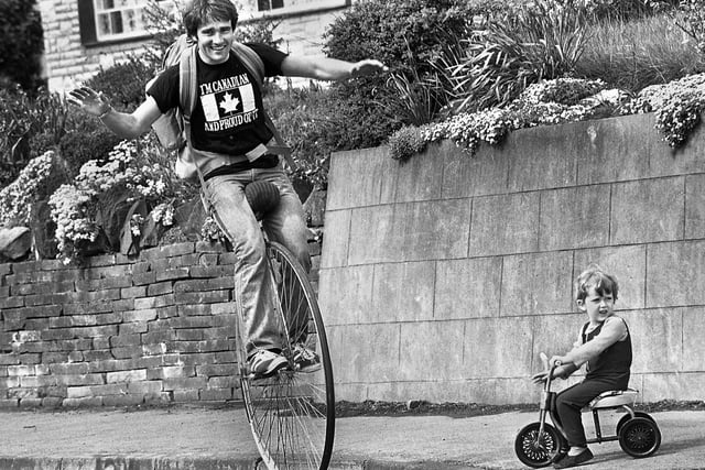 A Canadian uni-cyclist known as Wobbling Wally Watts pedals his way along Ashton Road, Newton-Le-Willows, watched by 3 year old Patrick Morgan on his three wheeled trike on Wednesday 5th of May 1976. Wally was on the English leg of a round the world trip by uni-cycle eventually covering 12.000 miles between 1976 and 1978.