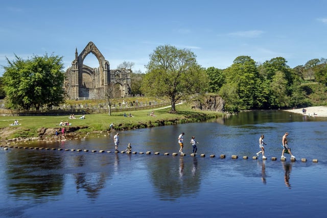 People enjoy the hot weather as they cross the River Wharfe near Bolton Abbey in North Yorkshire
