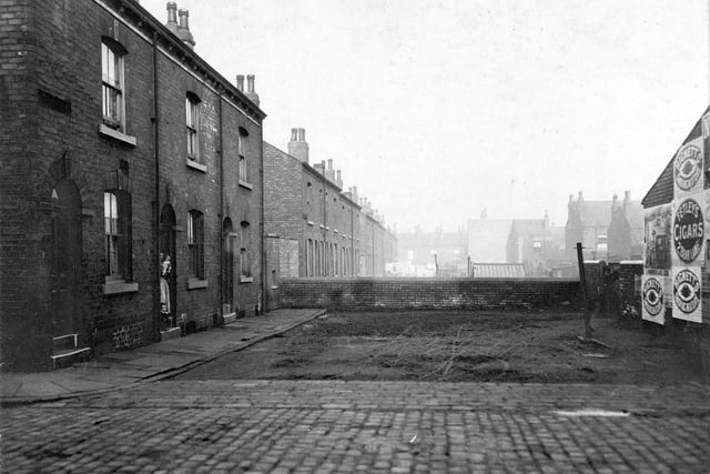 Disraeli Place in Hunslet. Pictured are three 'two up two down' terrace houses - a woman holds a baby in the doorway of the middle house.