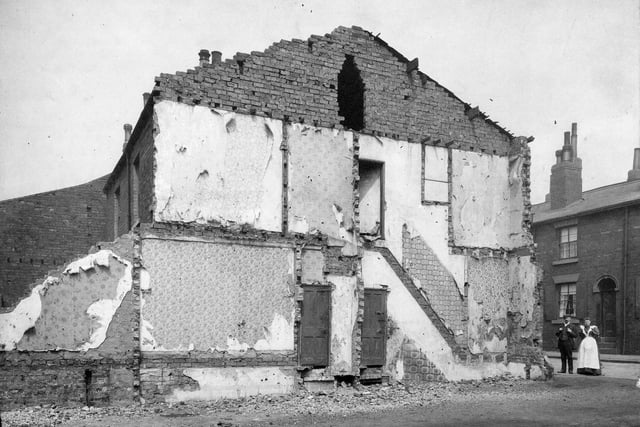 Terrace houses on Burmantofts Street which are partially demolished. Part of a terrace can be seen on the right hand side of the picture and in front is a man and a woman.