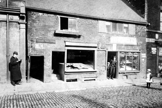 Kirkgate showing entrance to Cherry Tree Yard. A confectioners is on the right. The streets are paved with stone sets and tramlines.