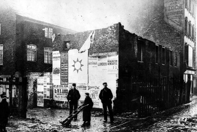 Lands Lane, east side, during demolition for street widening, showing entrance to Wheatsheaf Yard. A boy is holding a hand cart and three other men stand by. There is an advertisement on the wall for Leeds City Varieties.