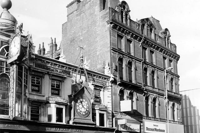 West side of Briggate. On the left is John Dyson & Sons, Jewellers and Watchmakers, which has two ornate clocks, one displaying the year 1865 in which the business was founded.