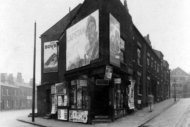 A corner shop at junction of Park Lane and Burley Street. Shop is covered in posters and advertising hoardings.