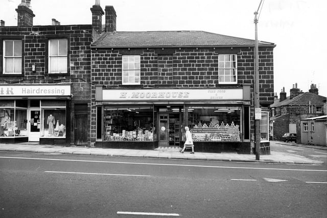 Otley Road, with the junction with Cottage Road on the right. Pictured is H. Moorhouse, grocers, and Mayfair Fashions and Hairdressing. A woman is walking past the grocers.