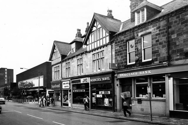 Shops on Otley Road including Woodcock Travel Agents and Bradleys Video and TV Centre. The Arndale Centre can be seen on the left, past the Wood Lane junction, with Arndale House towering in the background.