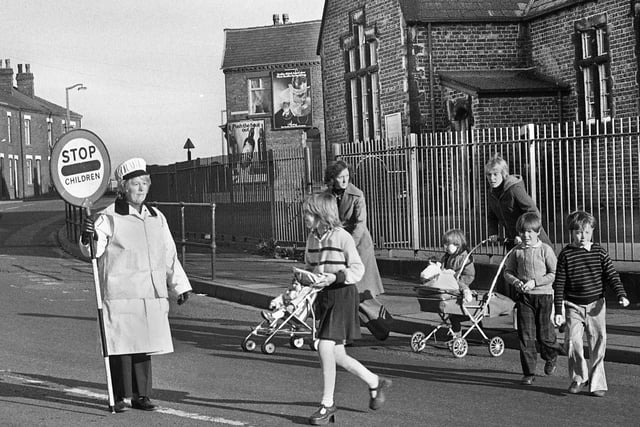 Lollipop lady Mrs. Hargreaves shepherds kids and parents across the road from the old St. Nathaniel's Primary School on Liverpool Road, Platt Bridge in 1976.