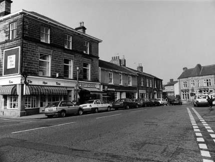 A view looking across the Market Place towards a row of shops. These include The Shoe Tree footwear at no. 23 on the left, beside the junction with Scott Lane, then Provender delicatessen at 23a and Yorkshire Electricity Board.