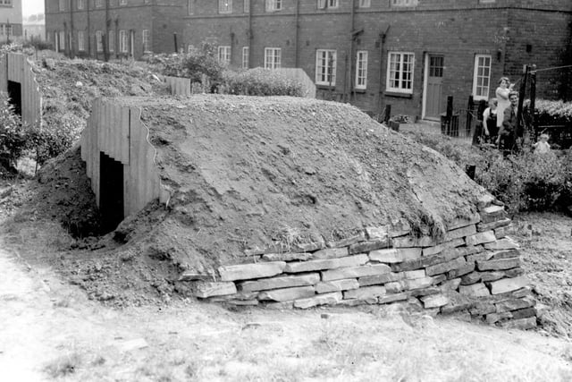 Anderson Shelter put up for no. 73 Wykebeck Avenue, reinforced by stone wall and earth. On the right a woman and children are watching the camera man.