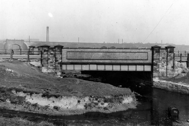 A stone, brick and iron bridge over Low Beck. South side of bridge looking North. In the background is a subway beneath the railway bridge leading to Oswald Grove.