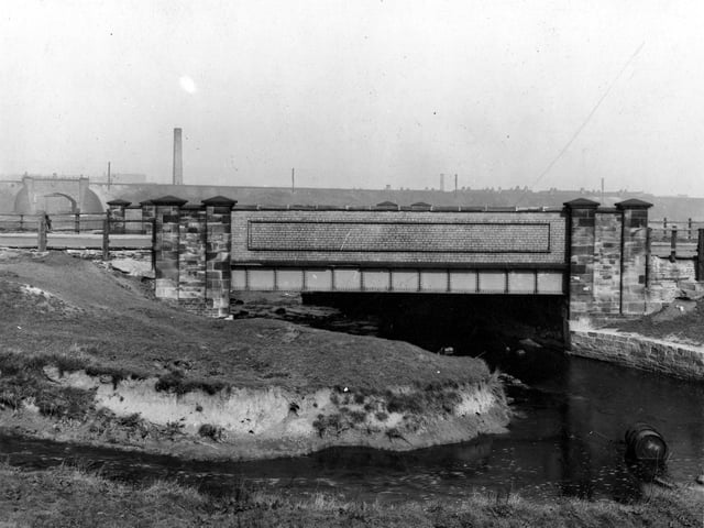 A stone, brick and iron bridge over Low Beck. South side of bridge looking North. In the background is a subway beneath the railway bridge leading to Oswald Grove.