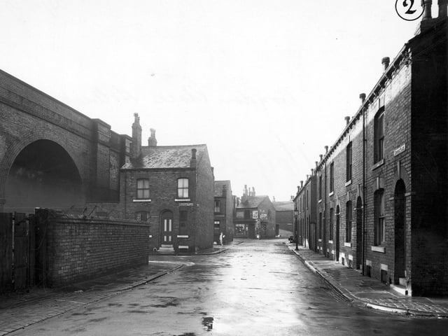 A view along Croydon Place with Domestic Street Bridge, Staincross Place and Staincross Street on the left. A tobacconists can be seen in the background. A woman and a streetlamp are visible.