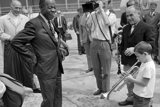 Young Enrico Tomasso greets Louis Armstrong at Leeds Bradford Airport with a tune on his trumpet - and the great Satchmo listens critically. Louis Armstrong and the All Stars were appearing at Batley Variety Club.