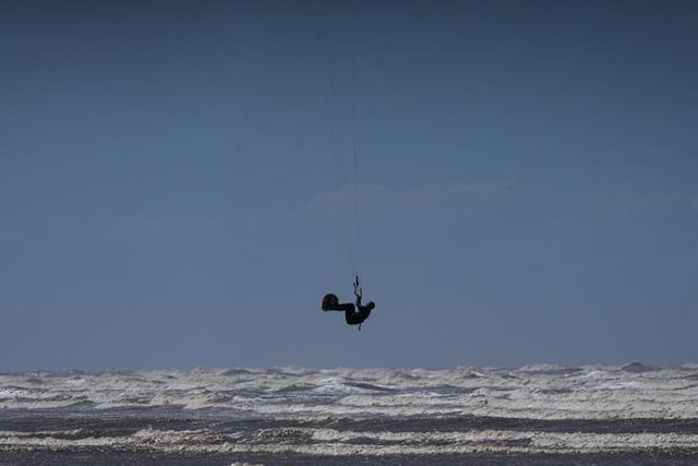 A kiteboarder harnesses the power of the wind with a large controllable power kite to be propelled across the water, land, or snow