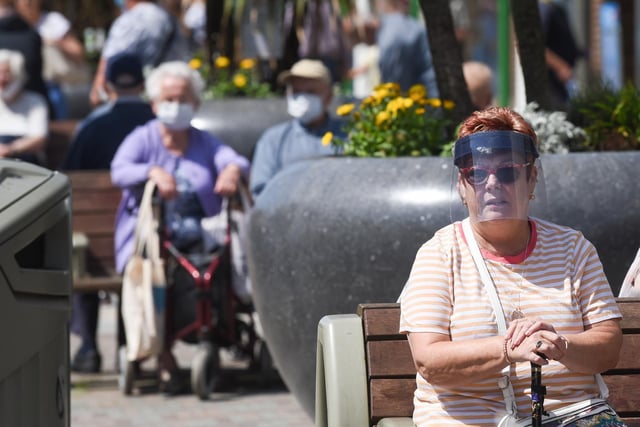 Shoppers take a breather from the heat on the high street's benches in masks and visors.