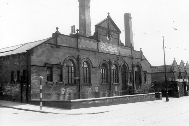 The premises of Montague Burton, The Tailor of Taste, showing building with large arched windows and two chimneys in the background.