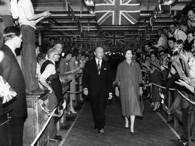 HM Queen Elizabeth II during a visit to the factory in October 1958. She is walking alongside company chairman Lionel Jacobson while workers applaud her on both sides with Union Jacks unfurled above