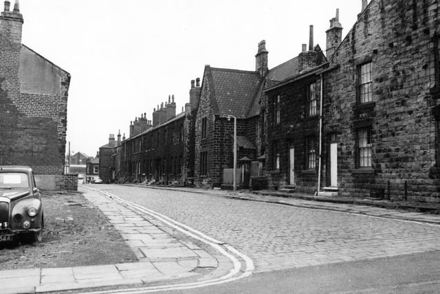 A view looking along Oddfellow Street in August 1968 from the junction with Wesley Street towards Fountain Street. A block of terraced houses have been demolished on the left and a car is parked in the waste ground.